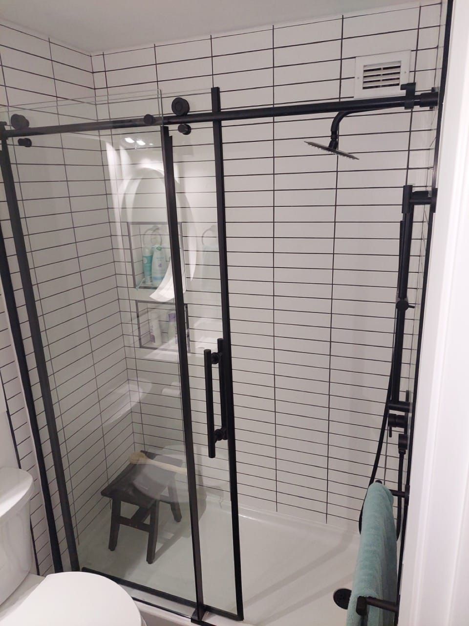 Dawn's renovated bathroom with white stacked tile, black fixtures and a glass sliding shower door